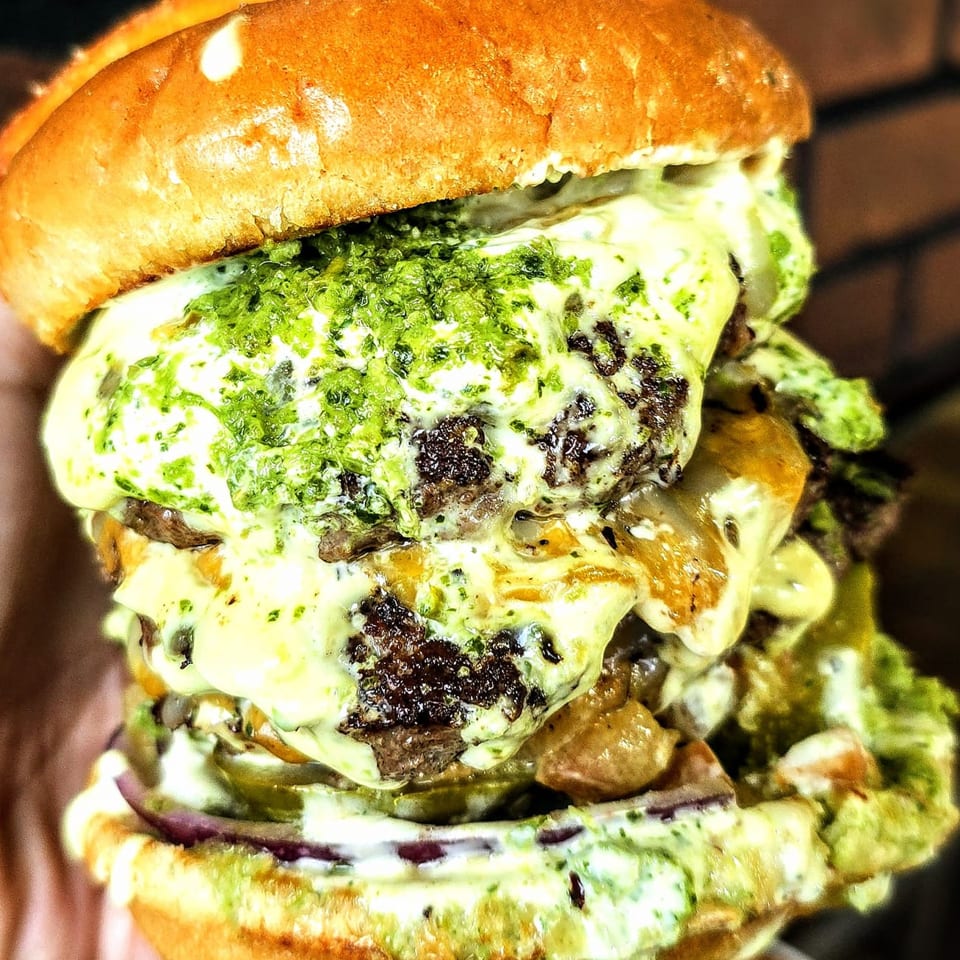A towering Burger Xpress burger with multiple patties, melted cheese, and green relish.